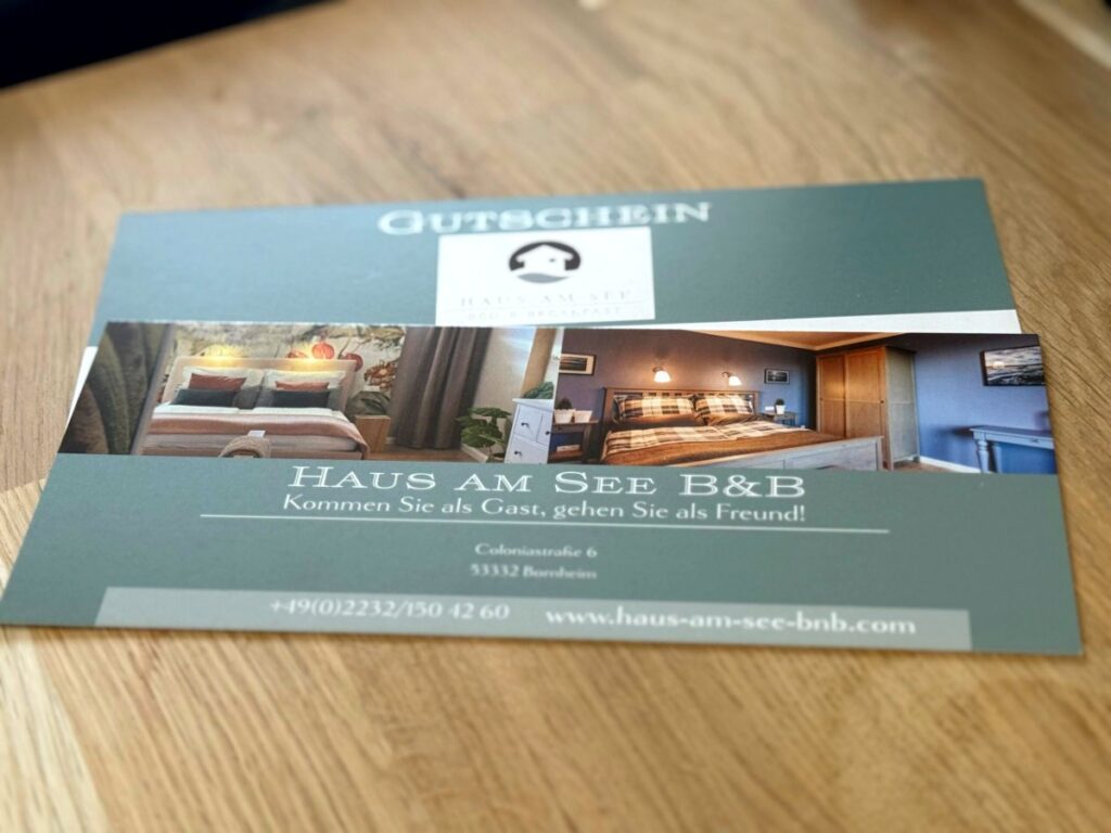Gutscheinkarte des Haus am See B&B mit Zimmerfotos auf einem Holztisch