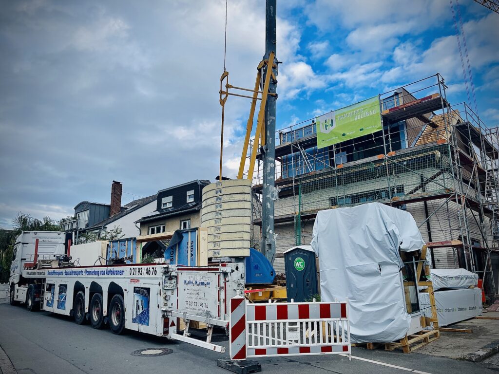 Umbau am Haus am See: der Bestand aus weißem Klinker, darüber der neue Aufbau aus Holz, am Gerüst ein Banner von Hamacher Holzbau
