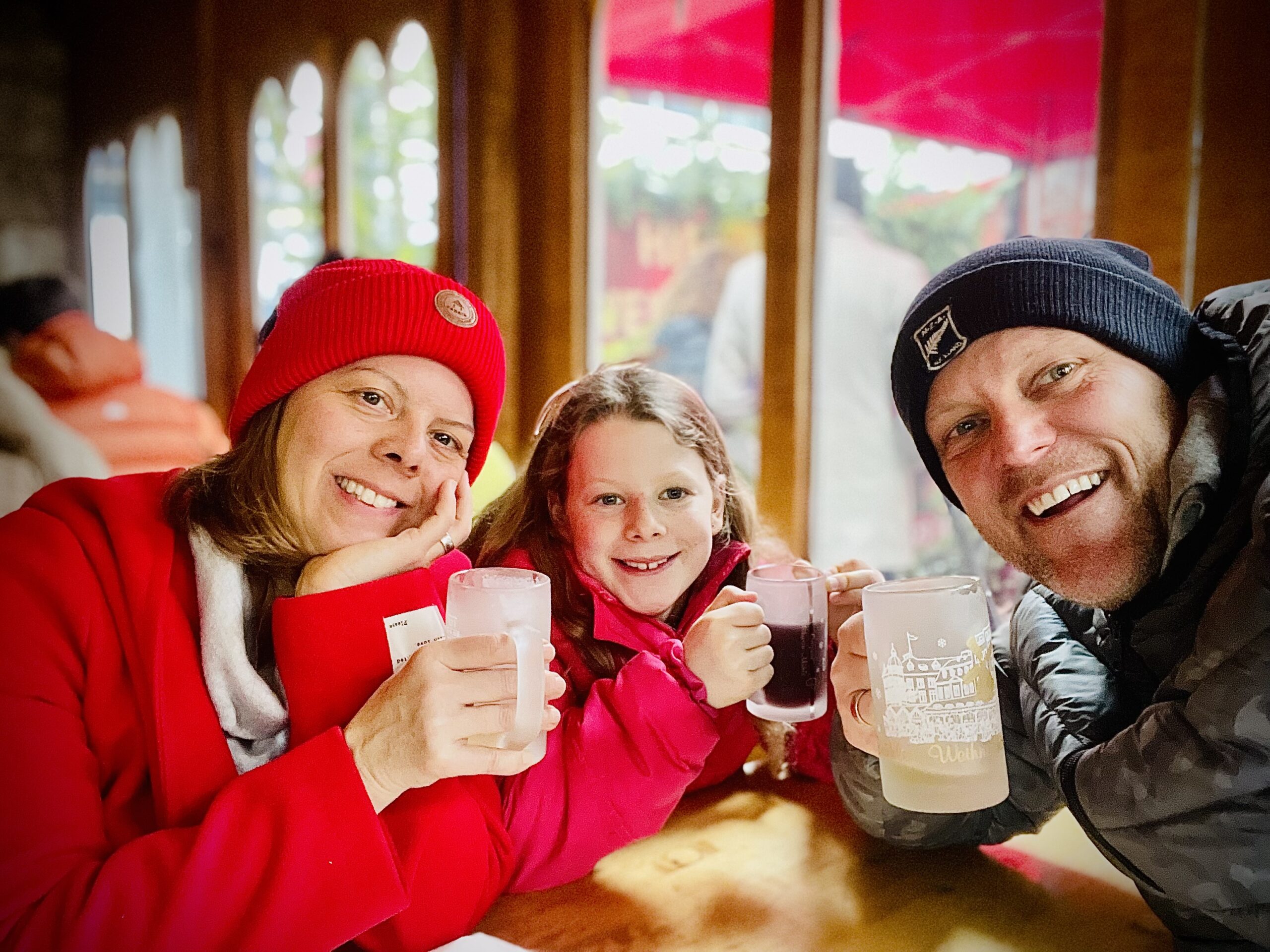 Simone und Sascha mit einem Kind und Tassen an einem Holztisch auf dem Weihnachtsmarkt